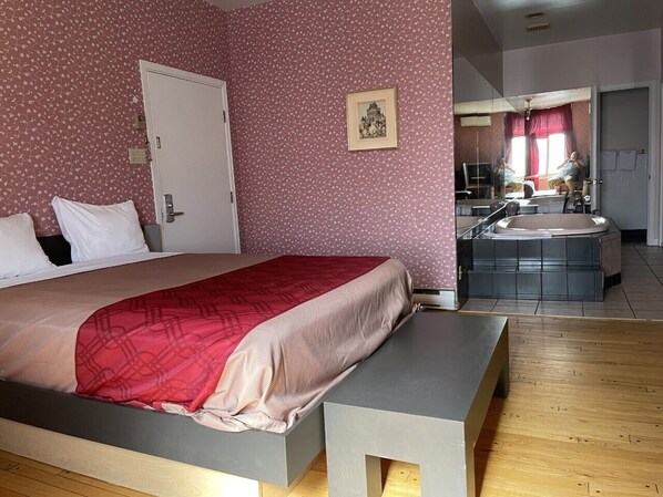 Un dormitorio con cama, un banco, un baño con bañera y un espejo.
