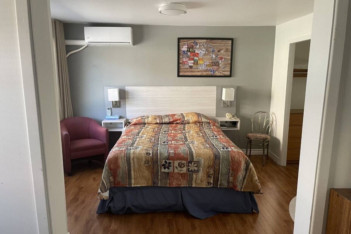 Une chambre à coucher comprenant un lit, une chaise, un bureau et un climatiseur fixé au mur.