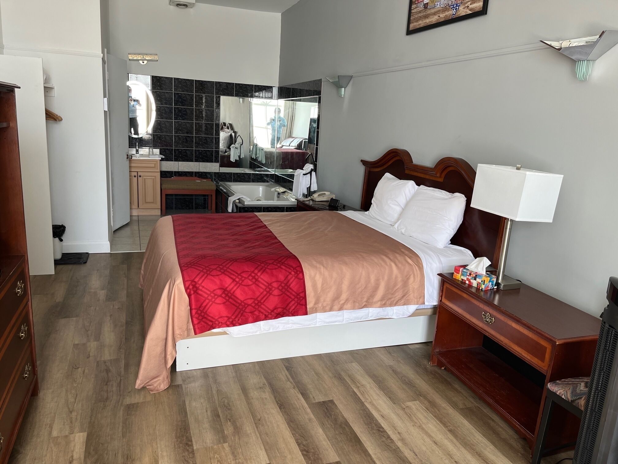 Habitación de hotel con una cama, una mesita de noche, un escritorio, un espejo y un baño visible a través de una puerta abierta.