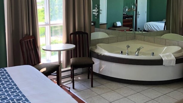 A hotel room with a large bed, a round jacuzzi, a small table, and a chair.