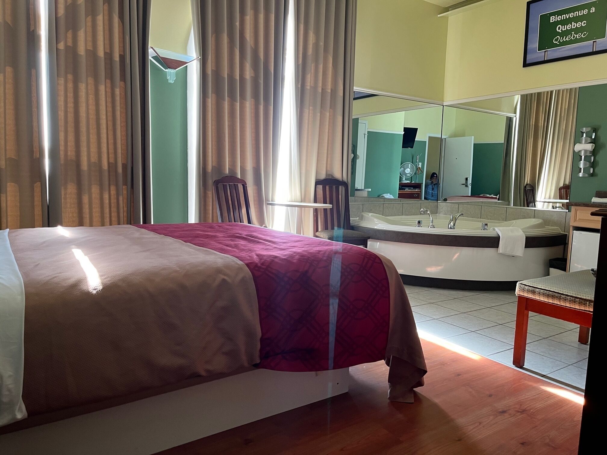 A hotel room with a bed, a bathroom with a bathtub, a mirror, and a sign that says "Bienvenue a Quebec Quebec".