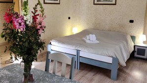 Una habitación de hotel con una cama, mesitas de noche, una mesa con sillas y un jarrón de flores.