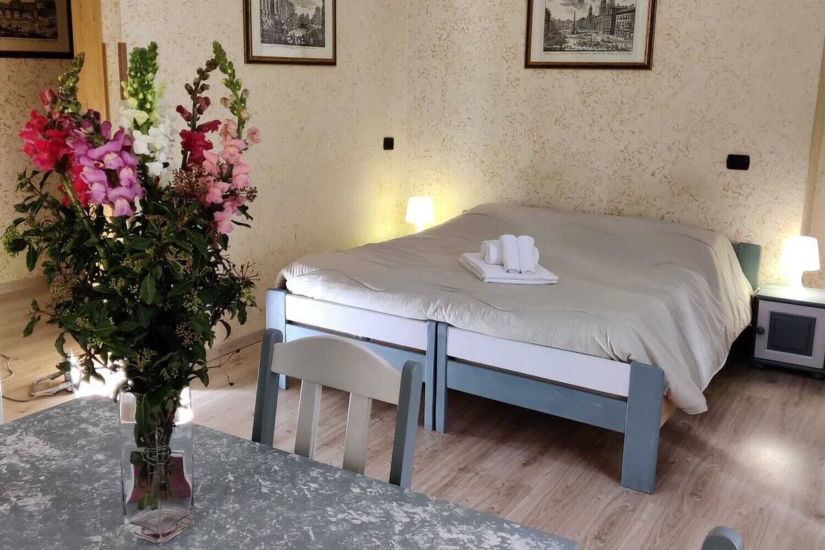A hotel room with a bed, bedside tables, a table with chairs, and a vase of flowers.
