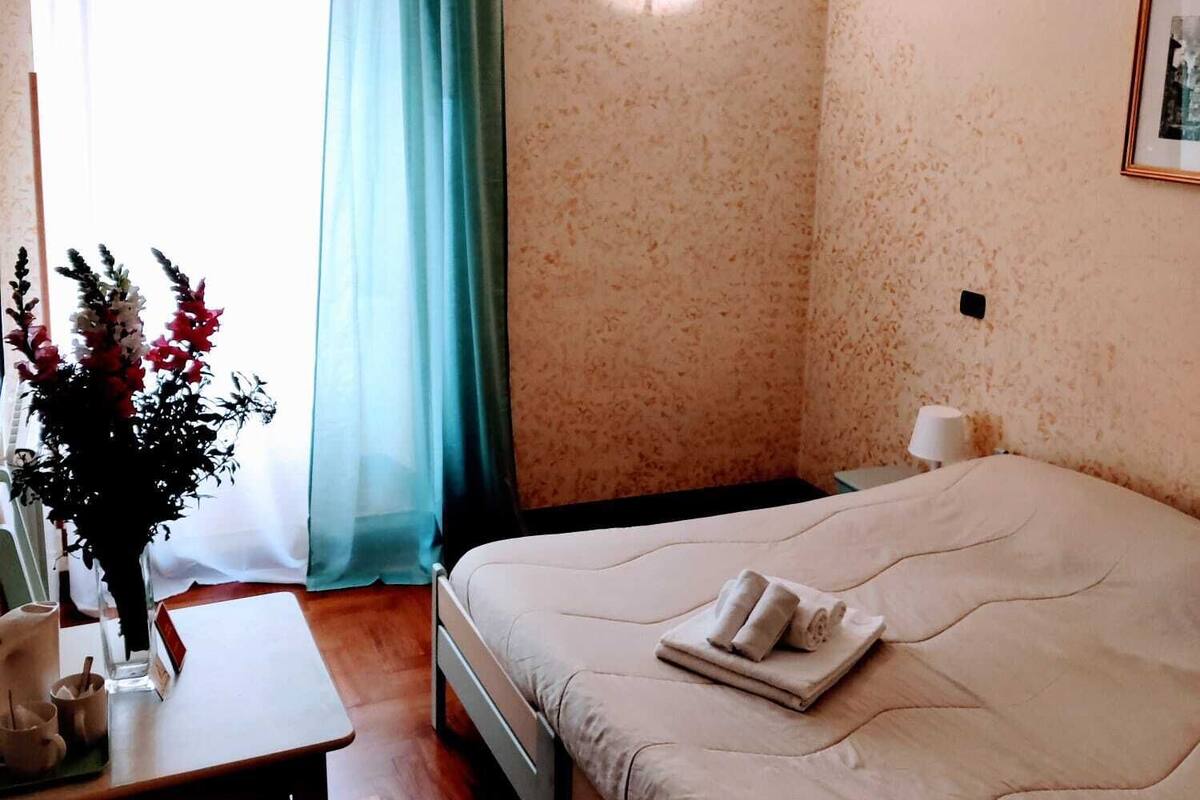 A hotel room with a bed, a desk, a chair, a lamp, and a window with curtains.