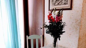 Una habitación pequeña con una puerta de madera, un cuadro enmarcado en la pared, una mesa con un florero y una silla.
