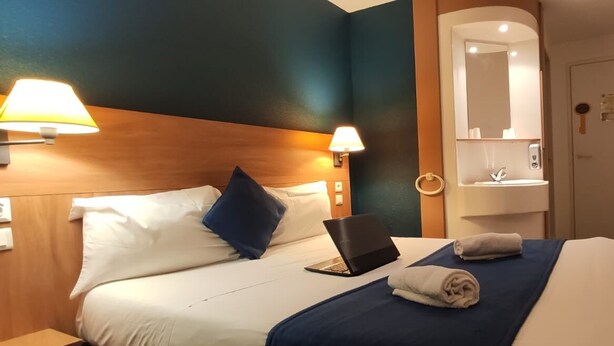 A hotel room with a bed, a laptop, a towel, a nightstand, and a bathroom mirror. - Glisy Hotel (Glisy)