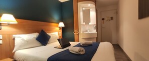 A hotel room with a bed, a laptop, a towel, a nightstand, and a bathroom mirror. - Glisy Hotel (Glisy)
