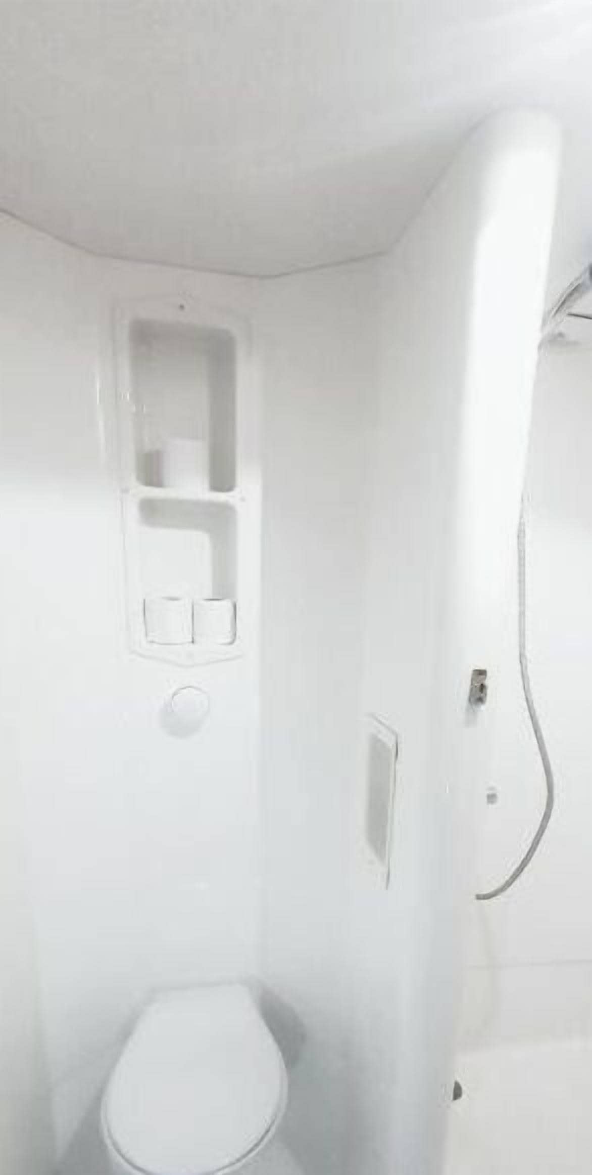 Une petite salle de bain blanche, équipée de toilettes, d’un lavabo et d’un espace douche.