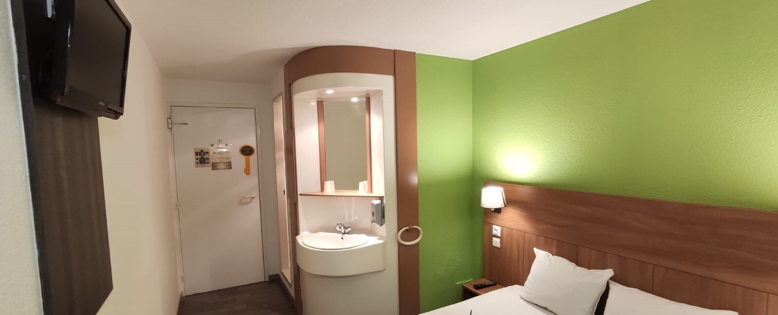 Een hotelkamer met een bed, nachtkastje, wastafel en televisie.