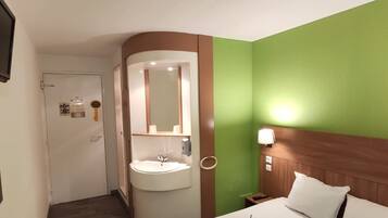 Een hotelkamer met een bed, nachtkastje, wastafel en televisie.
