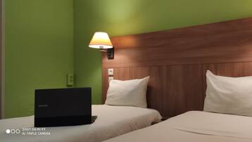 A hotel room with two beds, a wooden headboard, bedside lamps, and a laptop on the left bed.