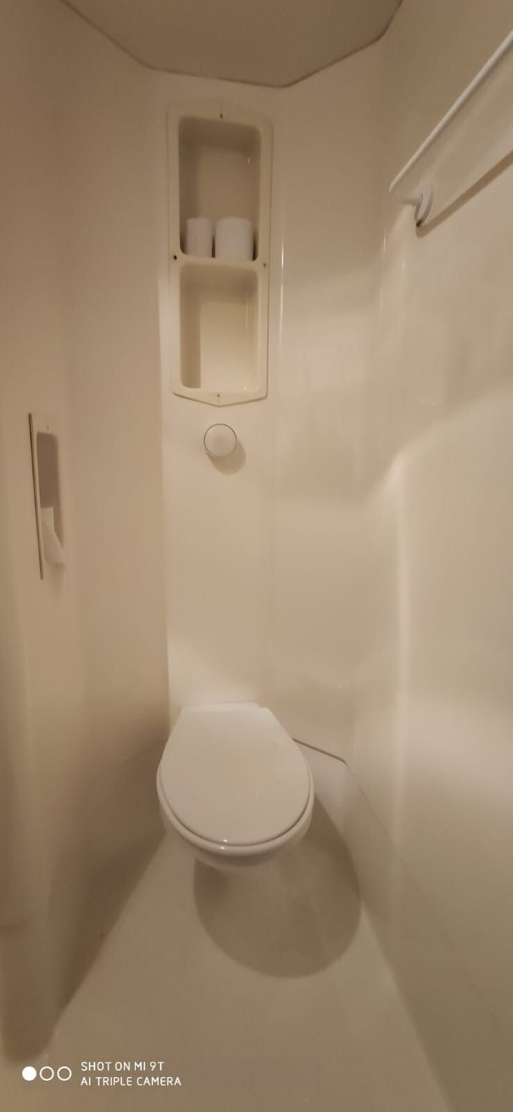 Un bagno piccolo e bianco, chiuso, con un water, uno scaffale con carta igienica e un porta asciugamani.