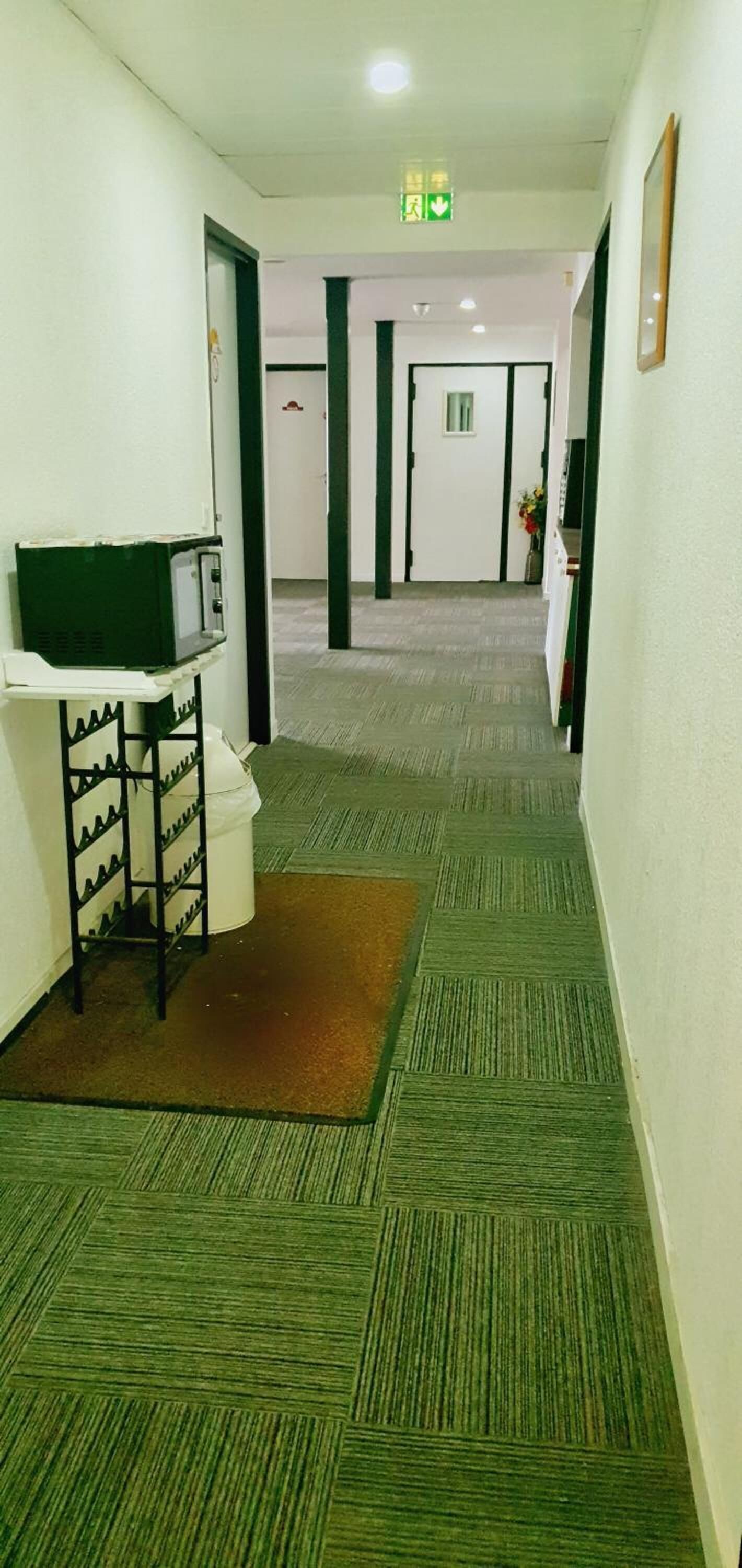 A hotel corridor with carpeted floors, a shoe rack, a trash bin, and a reception desk.