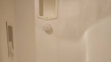A small, white, enclosed bathroom with a toilet, a shelf with toilet paper, and a towel rack.