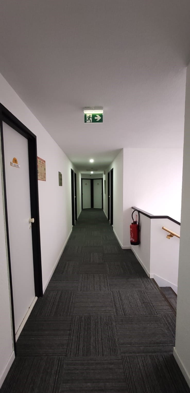 En korridor med en brandsläckare monterad på väggen, en grön utrymningsskylt och en dörr med en namnskylt.