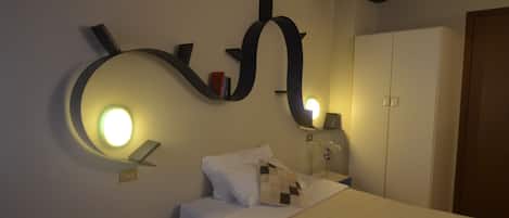 A bedroom with a bed, a nightstand, a telephone, a wall-mounted light fixture, and a wardrobe.