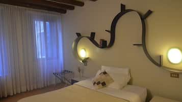 Une chambre d’hôtel avec un lit, un miroir fixé au mur, une table de chevet avec une lampe et une fenêtre avec des rideaux.