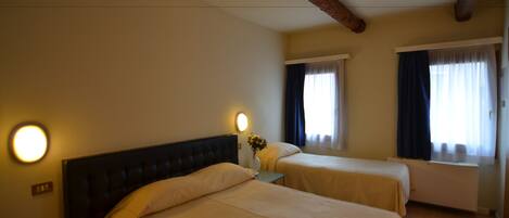 A hotel room with two beds, a nightstand with a vase of flowers, and a window with curtains.