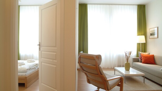 A hotel room with a bed, a chair, a sofa, a coffee table, and a lamp. - Aparthotel am Zwinger (Dresden)