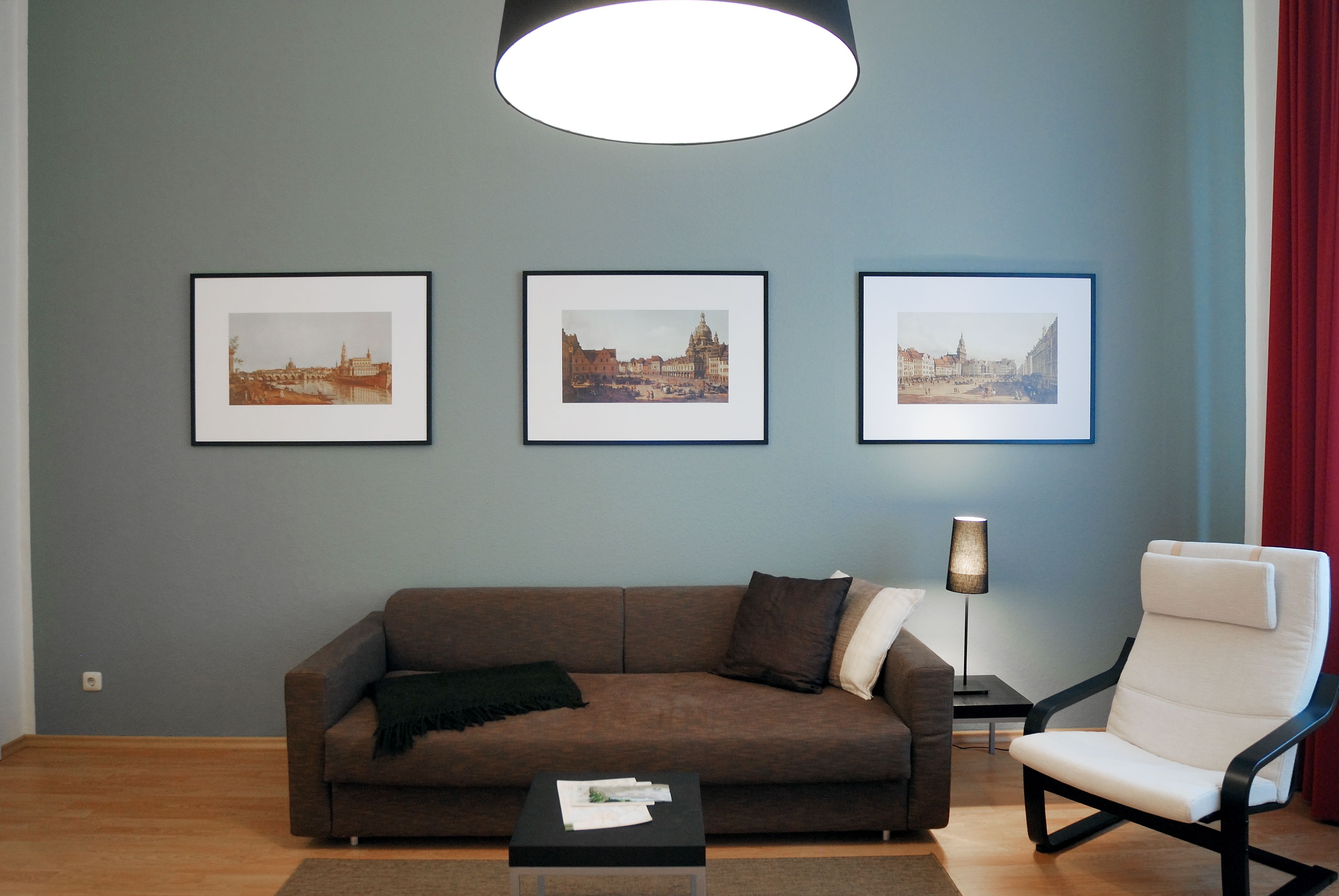 Ein Wohnzimmer mit einem braunen Sofa, einem weißen Sessel und drei gerahmten Bildern an der Wand.