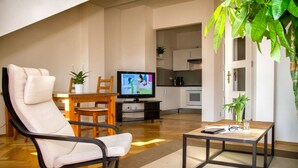 A modern living room with a reclining chair, a coffee table, a television, and a kitchen in the background. - Aparthotel am Zwinger (Dresden)