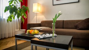 A living room with a sofa, a coffee table, a potted plant, a lamp, and a framed picture on the wall. - Aparthotel am Zwinger (Dresden)