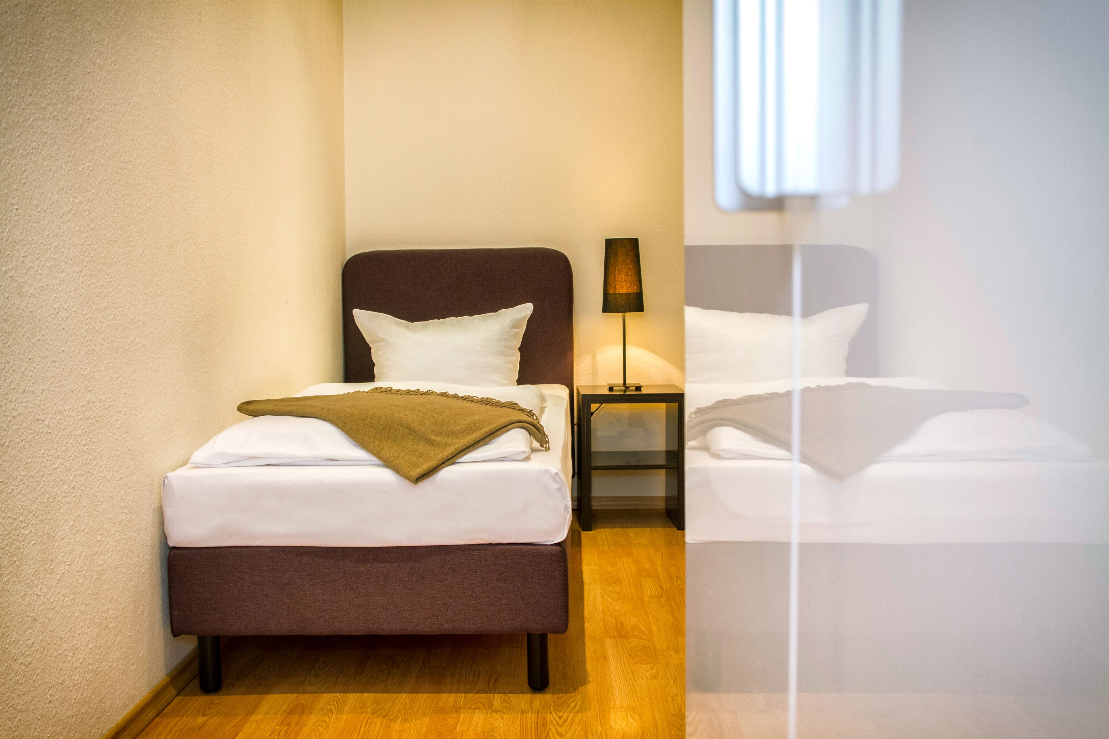 Et hotelværelse med to senge, et natbord med lampe og et vindue med persienner.