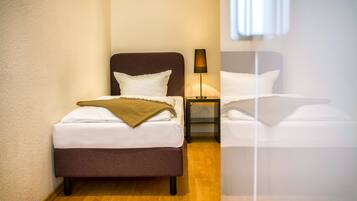 Et hotelværelse med to senge, et natbord med lampe og et vindue med persienner.