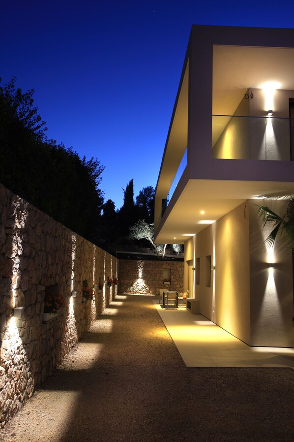 Un edificio moderno con una pared de piedra en un lado y un techo plano en el otro, con un interior bien iluminado y un cielo despejado.