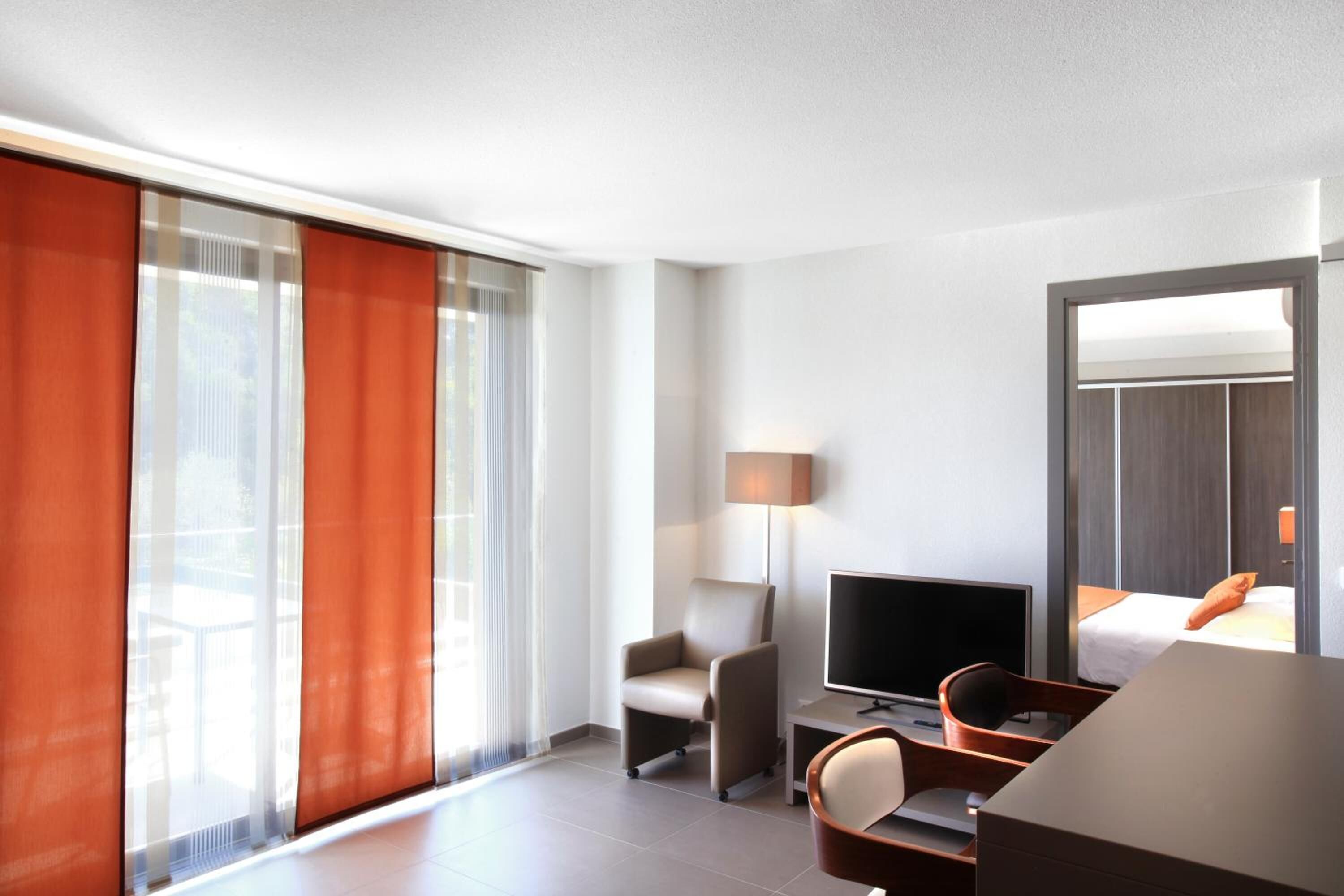 Una habitación de hotel moderna con un ventanal grande, un televisor de pantalla plana, un escritorio y una cama.