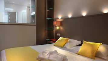 Una habitación de hotel con cama, almohadas, mesita de noche, lámpara y espejo.