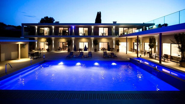 A modern hotel with a large outdoor swimming pool, multiple balconies, and well-lit outdoor seating areas. - Hotel Seventeen (Valbonne)