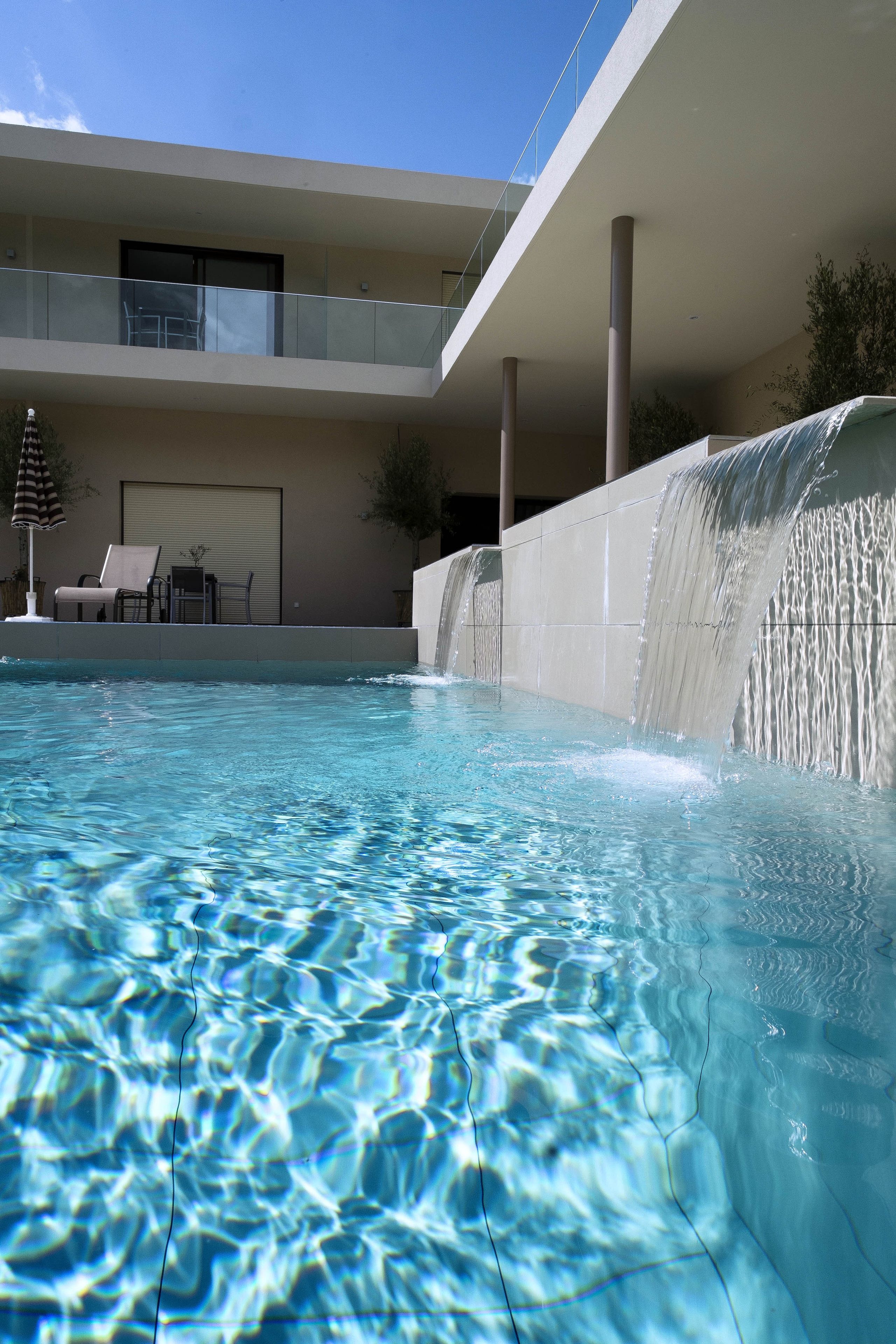 Una piscina con cascada, sillas de descanso y una zona de estar cubierta.