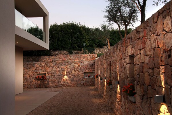 Un espacio exterior moderno con un muro de piedra, un balcón de cristal y plantas en macetas.
