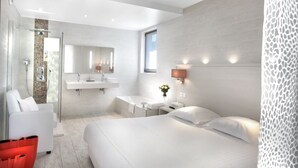 A modern hotel room with a large bed, a sitting area with a chair, a glass-enclosed shower, and a vanity with a mirror. - Hotel Seventeen (Valbonne)