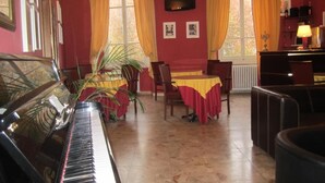 A room with a piano, dining table with chairs, a television, and a radiator. - Hotel Genzianella (Florence)