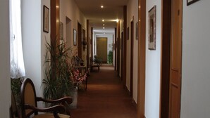 A long, narrow hallway with wooden doors and framed pictures on the walls. There are chairs and a potted plant along the left side. - Hotel Genzianella (Florence)