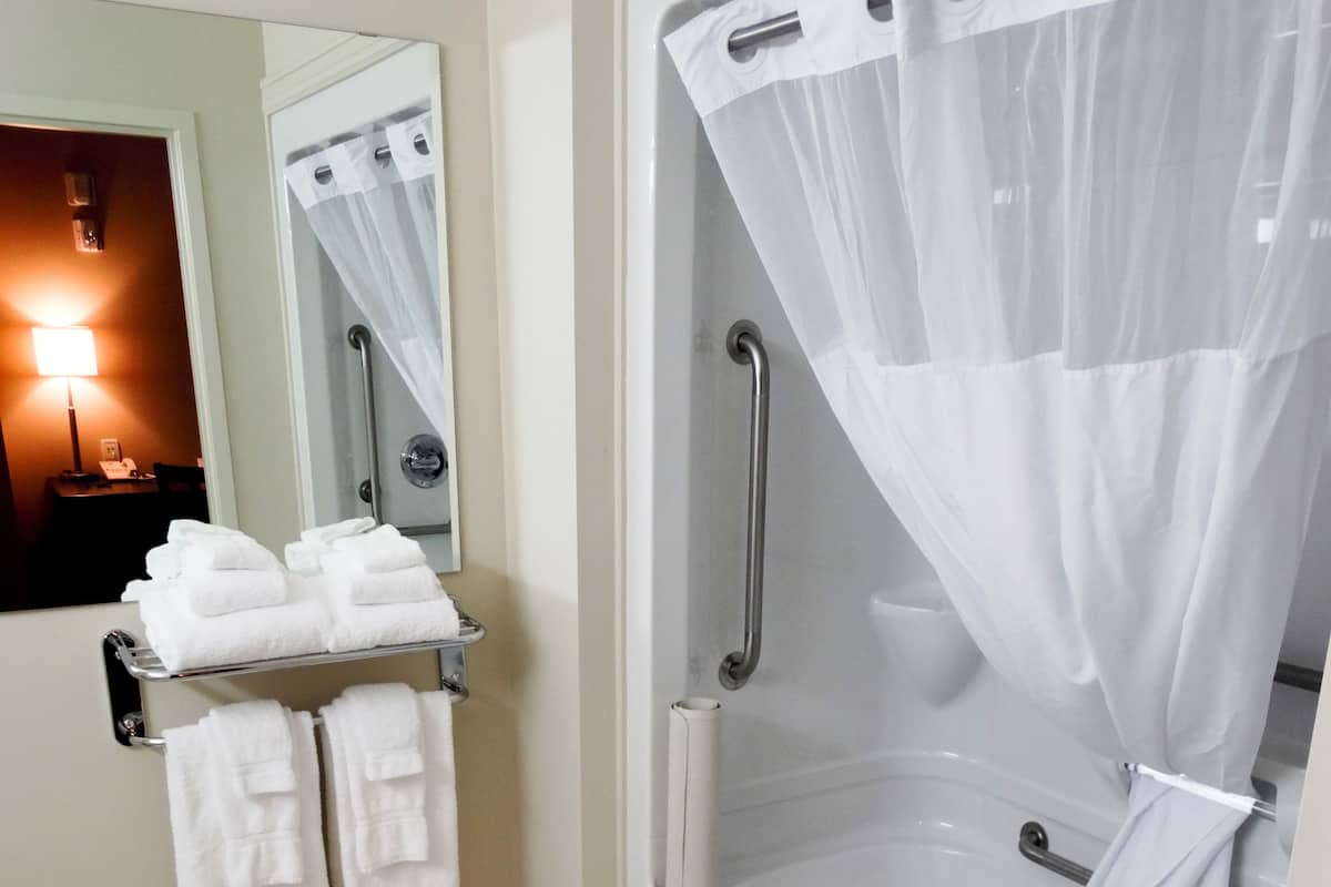 A bathroom with a bathtub, a towel rack with towels, a mirror, and a shower curtain.