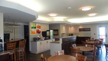 A modern kitchen with a central island, dining area with wooden tables and chairs, and a bar area with a refrigerator and microwave.