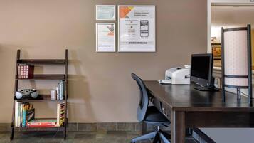 A hotel room with a desk, chair, bookshelf, and a large window.