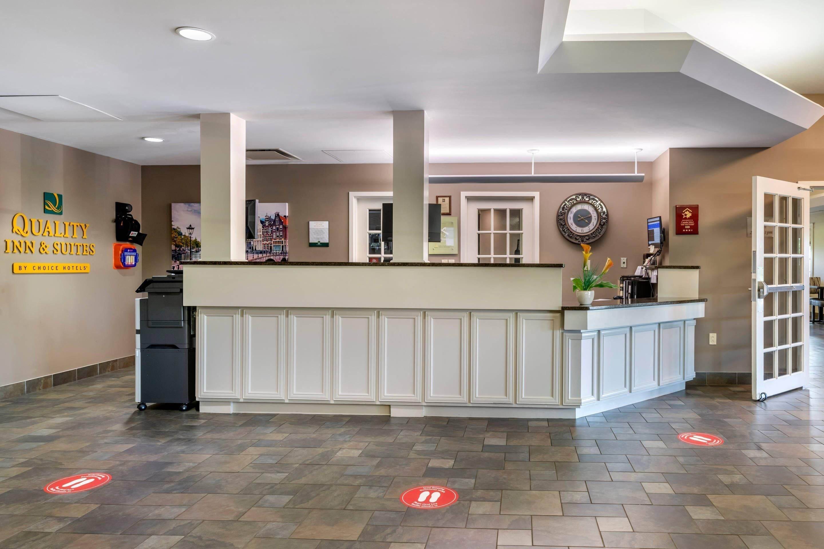Zona de recepción de un hotel con mostrador de recepción, un reloj y un cartel que dice 'Quality Inn & Suites by Choice Hotels'.