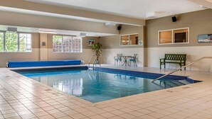 An indoor swimming pool with tiled flooring, a blue bench, and a small table with chairs. - Quality Inn & Suites Quispamsis (Quispamsis)