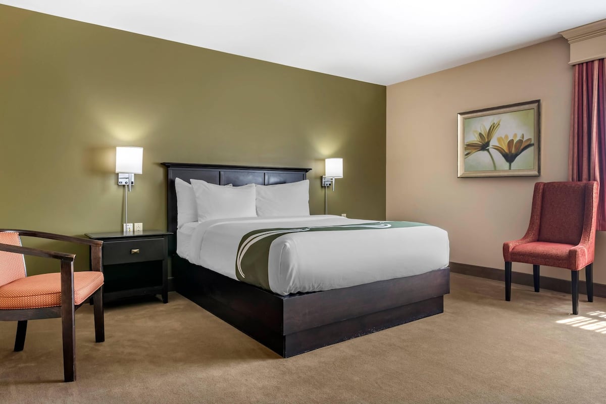 A hotel room with a bed, nightstands, a chair, and a painting on the wall.
