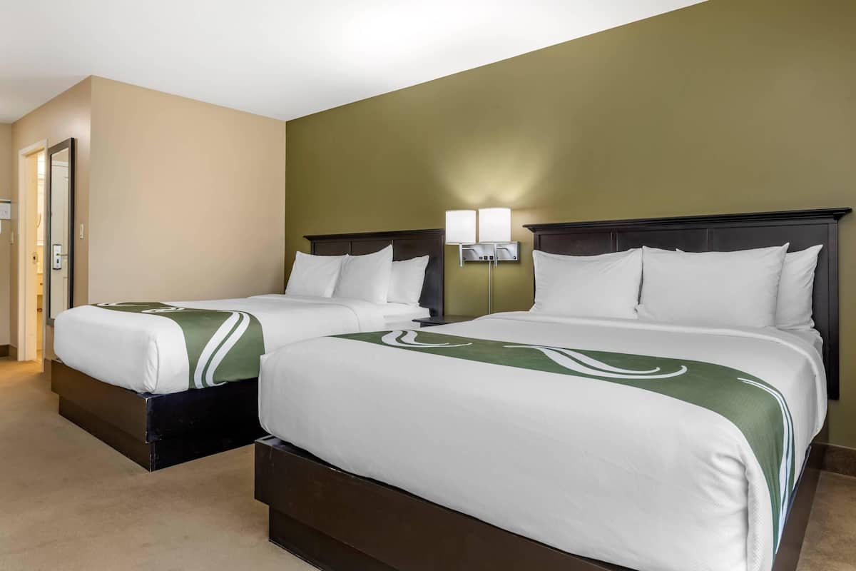 A hotel room with two beds, beige walls, and a green accent wall.