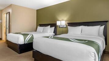 A hotel room with two beds, beige walls, and a green accent wall.