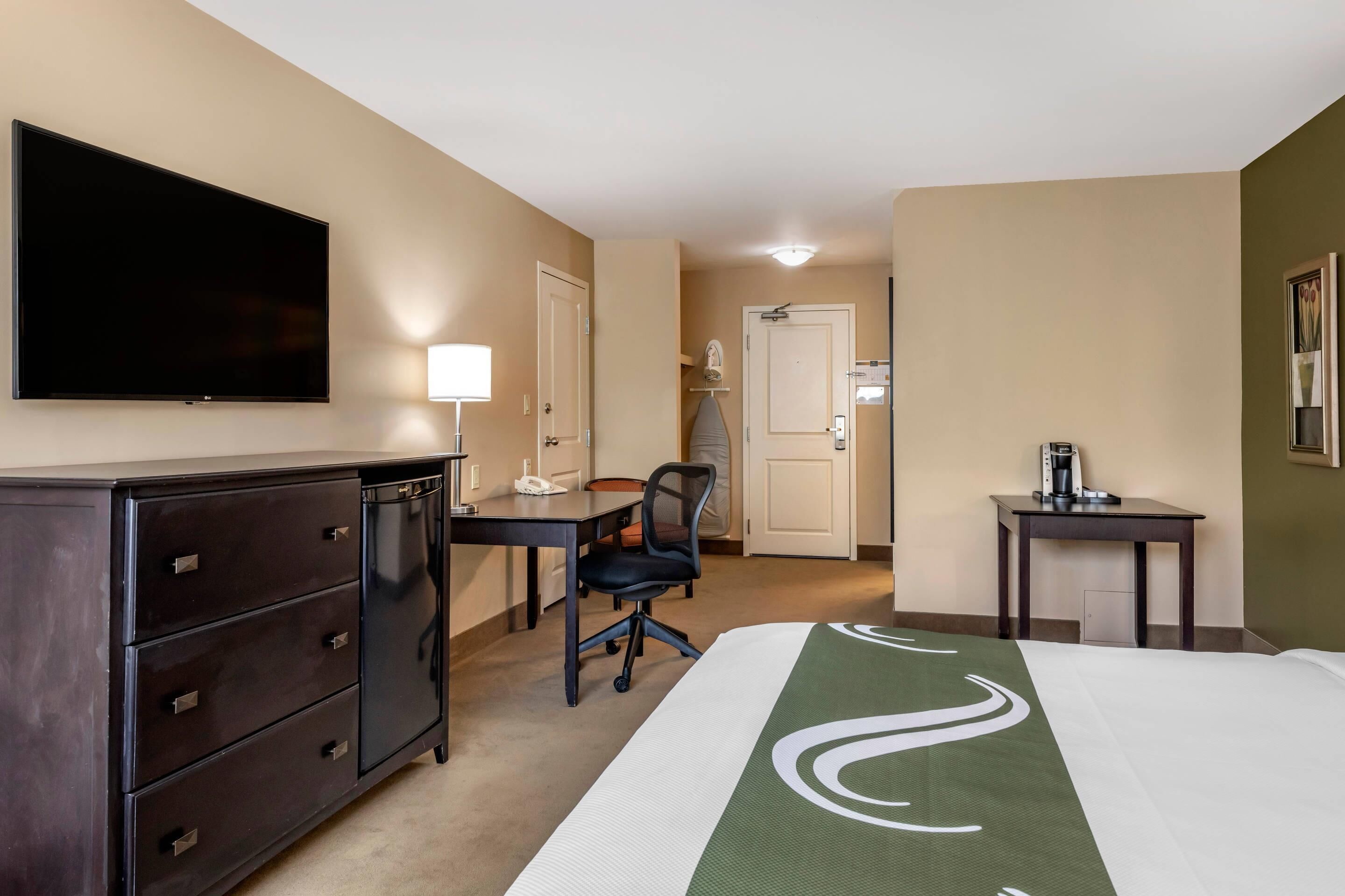 A hotel room with a bed, a desk, a chair, a dresser, a television, and a coffee maker.