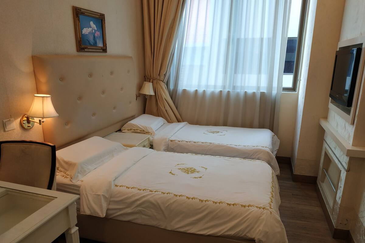 Quarto de hotel com duas camas, uma escrivaninha, televisão e um quadro na parede.