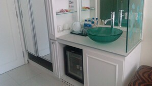Un baño con un lavamanos verde, armarios blancos y una cabina de ducha de cristal.