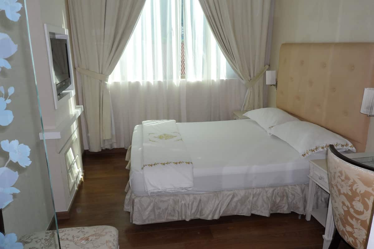 Quarto de hotel com uma cama grande, mesa de cabeceira, televisão na parede e janela com cortinas.