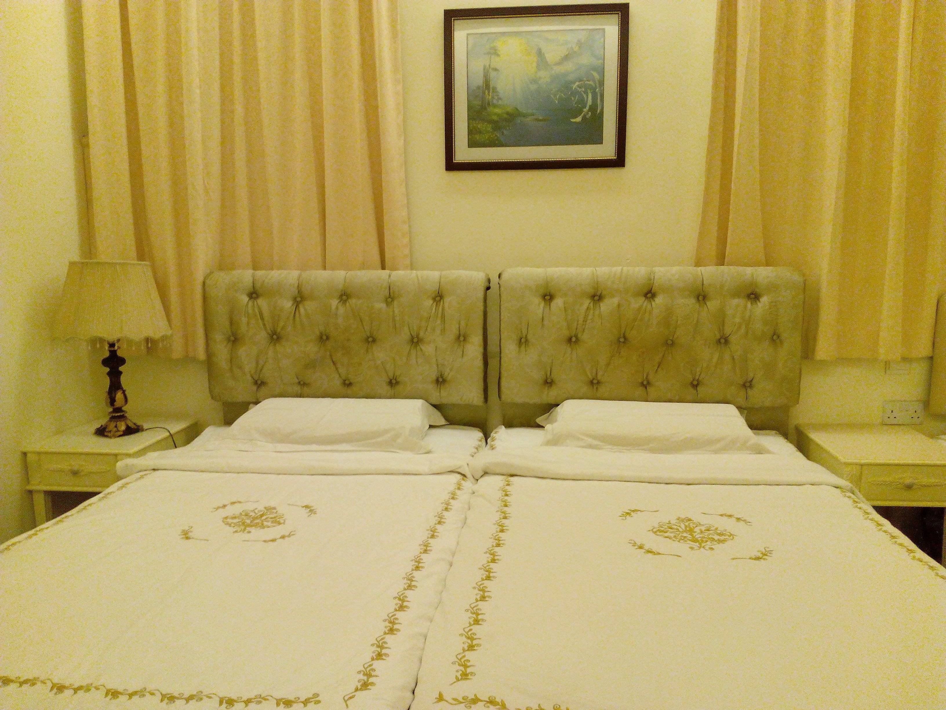 A double bed with a tufted headboard, two bedside tables, a lamp, and a framed painting on the wall.